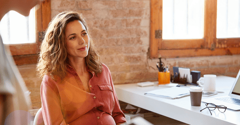 Pregnant businesswoman sitting by office desk looking away