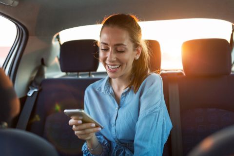 Smiling girl sitting in car with her mobile phone
