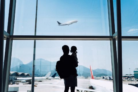 Father carrying daughter, looking out of airport window at a plane taking off
