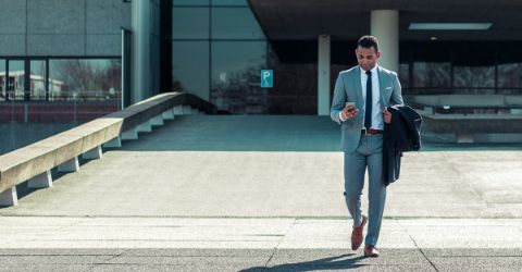 A man in a business suit with a mobile phone in his hands is leaving a building