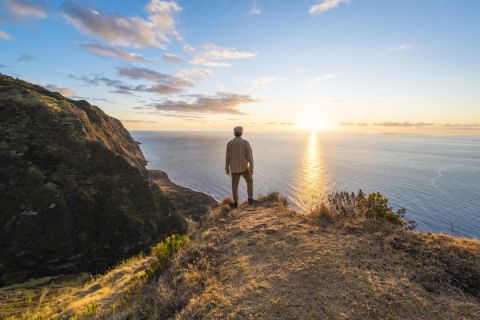 Man standing on cliff looking into sunset