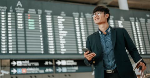 Smiling asian male traveler at airport using his mobile phone  
