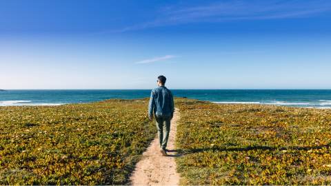 Man walking down sandy path to the sea