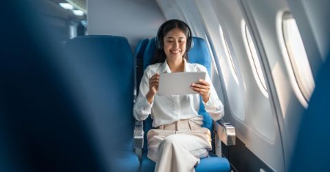 Young Asian business woman or female passenger wearing wireless headphone and working with tablet during the flight