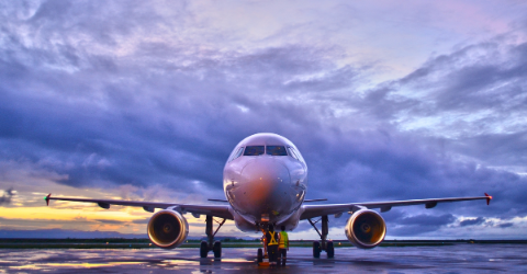A front-facing view of a commercial airplane on a wet runway at dusk, with dramatic purple and blue clouds in the sky and ground crew equipment visible beneath the aircraft.