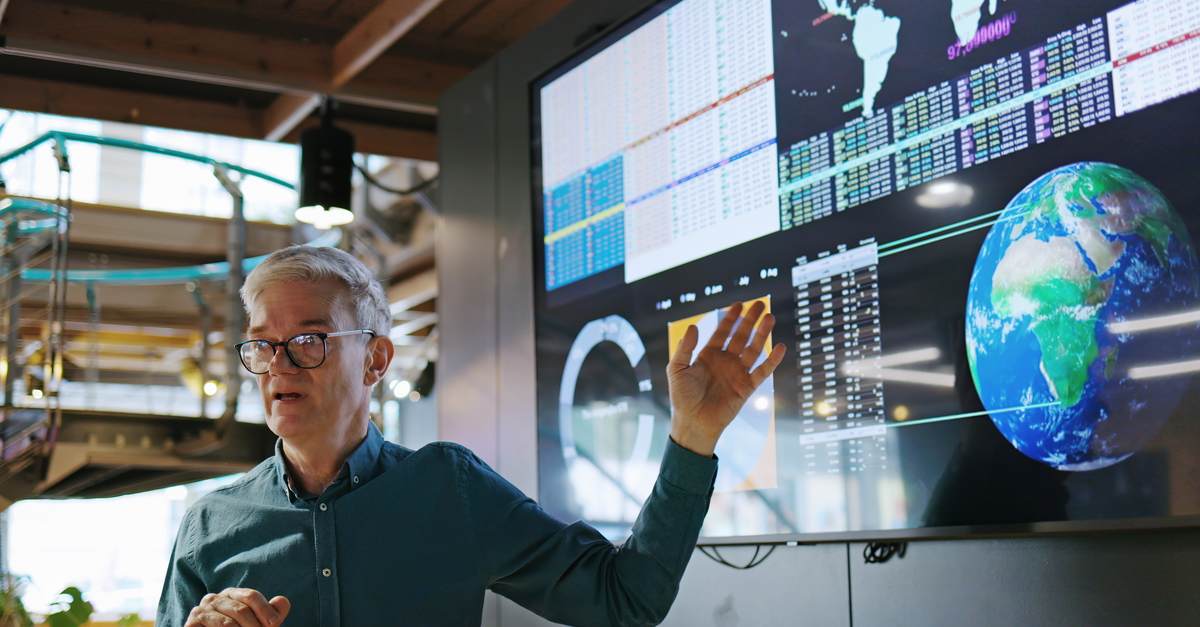 Man standing and gesturing towards a large screen displaying various data visualizations
