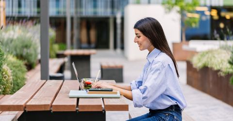 Woman having lunch outdoors while submitting her travel expenses.